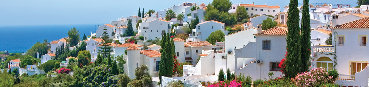 Properties on a hill top in Spain with the ocean in the background.